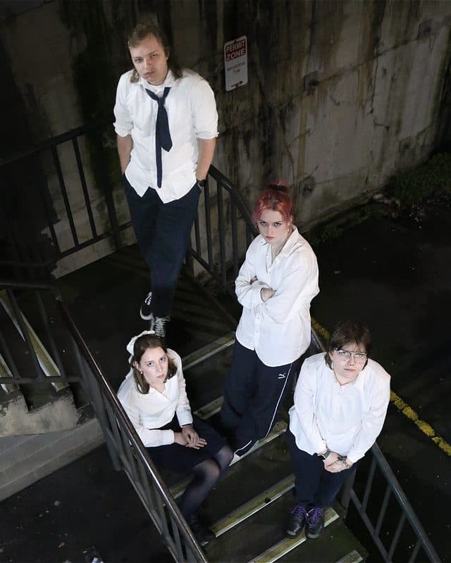 Four people on a grimey staircase in school uniforms look at the camera